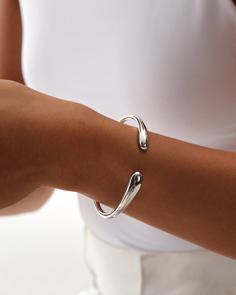 A Bangle in polished silver 316L stainless steel from Waldor & Co. One size. The model is Teardrop Bangle Polished.